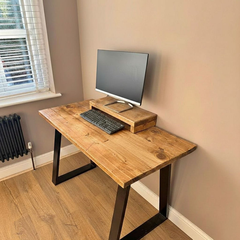 Wooden desk with computer setup in a room with a window and radiator.