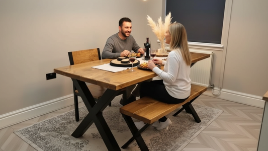 Man and woman sitting at a wooden dining table with a cake, in a home setting.